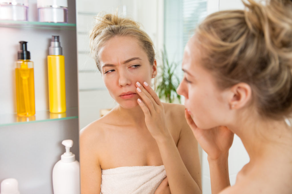 Woman examining her skin for dark circles in the mirror.