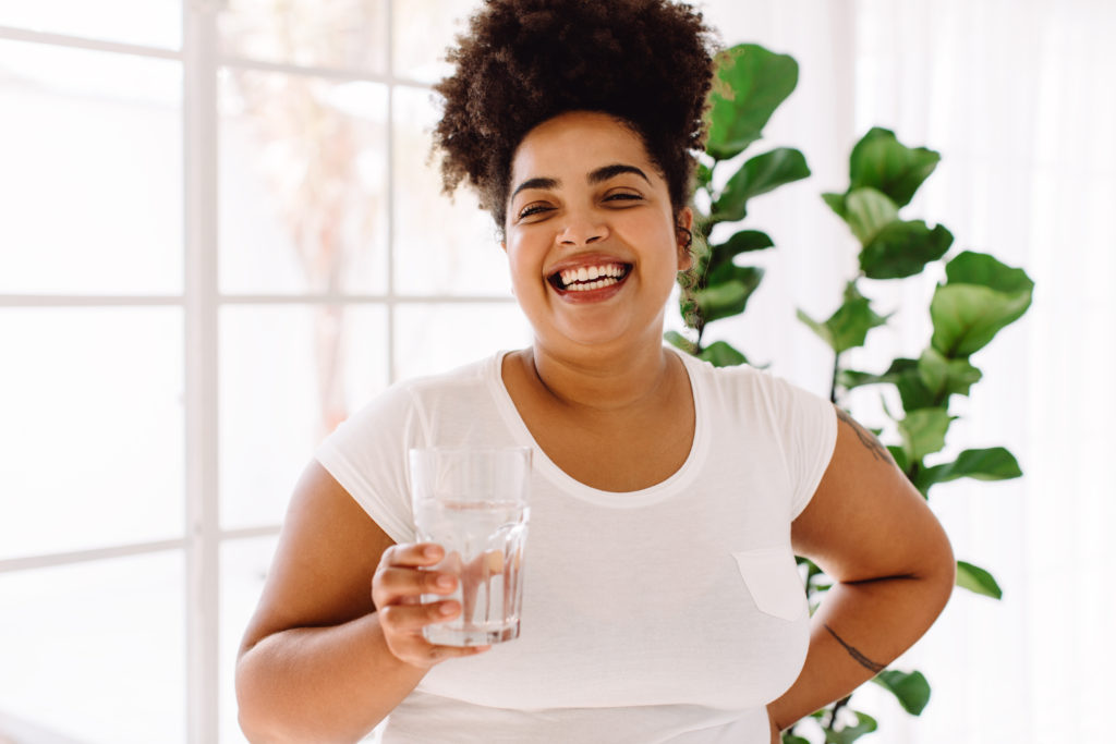 Woman drinking class of water while smiling.